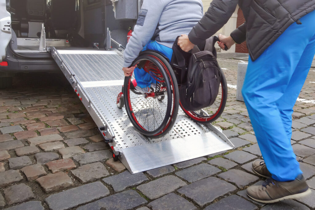 Man pushing a person on a wheelchair up a ramp to board a vehicle