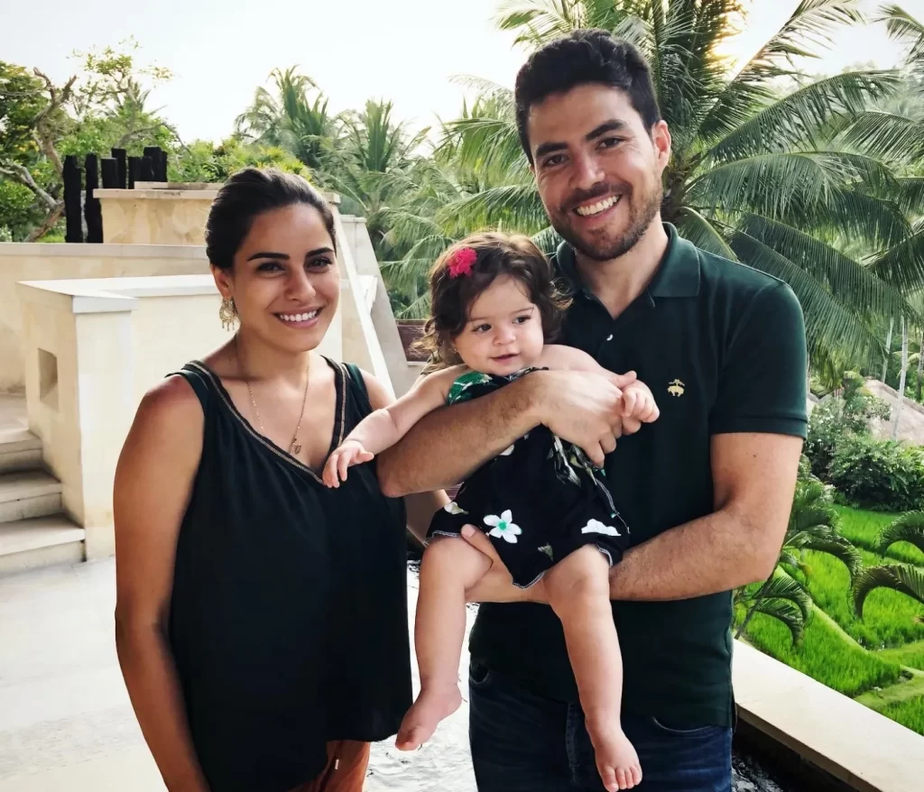 A woman and her husband holding their daughter in his arms while on a vacation in Bali