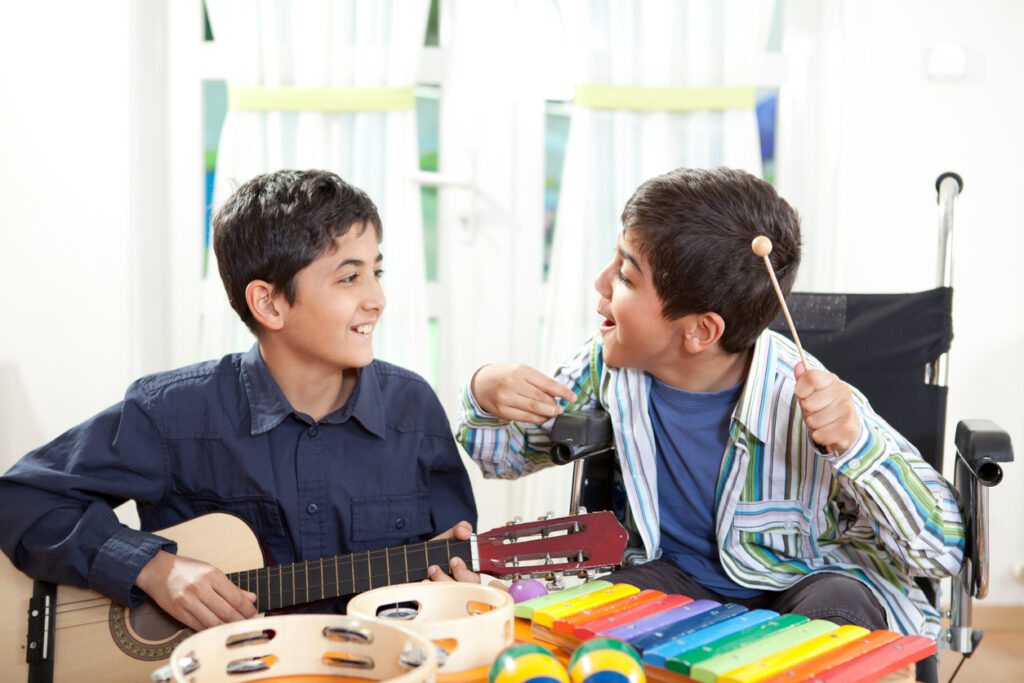 Two children playing with musical instruments, one is holding a guitar and the other playing a xilophone